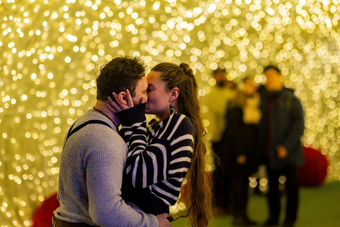 Ava and Bran kissing in front of a wall of golden lights